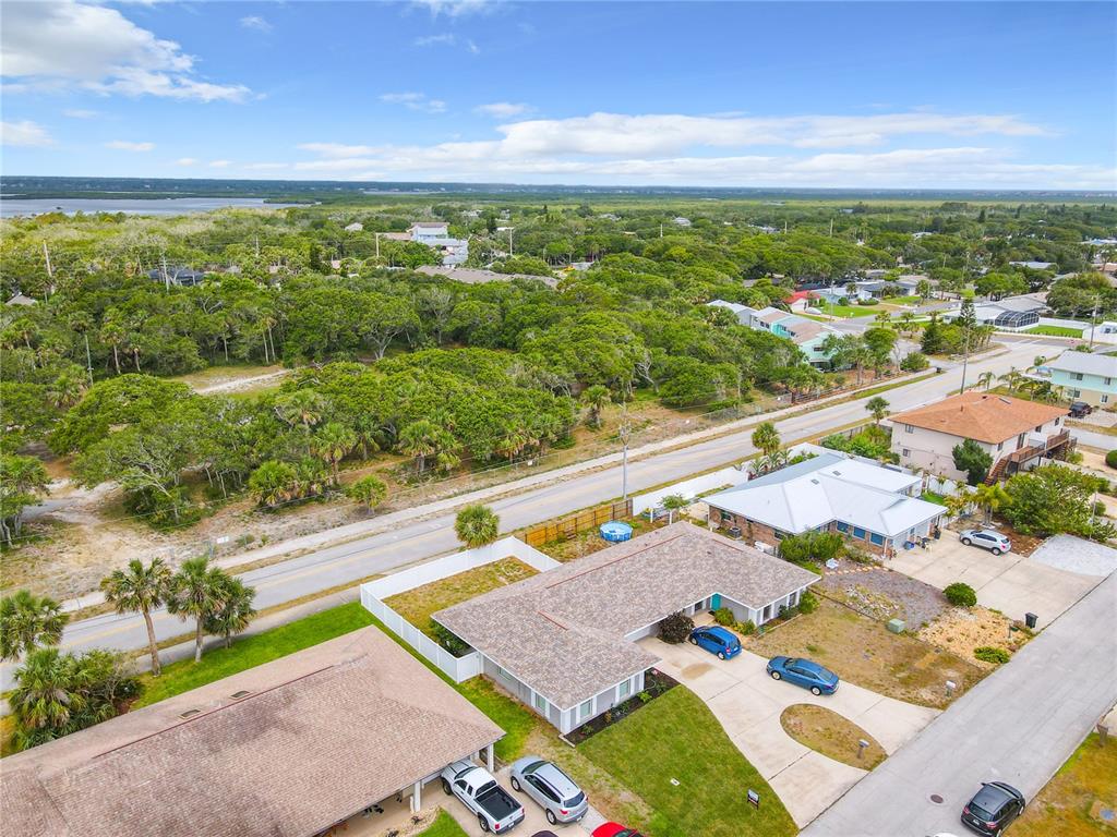 An aerial view shows a residential neighborhood with houses, driveways, and a road near trees — 3828 SANDSTONE COURT, NEW SMYRNA BEACH, FL