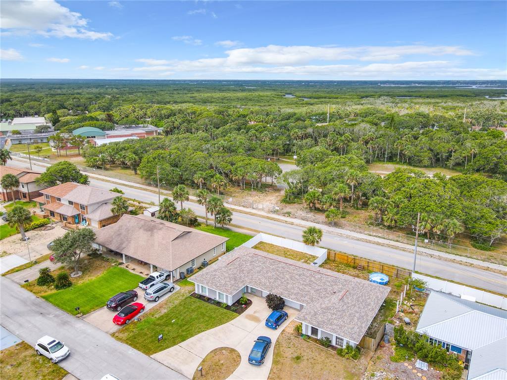 An aerial view shows a residential neighborhood with houses, driveways, and surrounding wooded areas — 3828 SANDSTONE COURT, NEW SMYRNA BEACH, FL