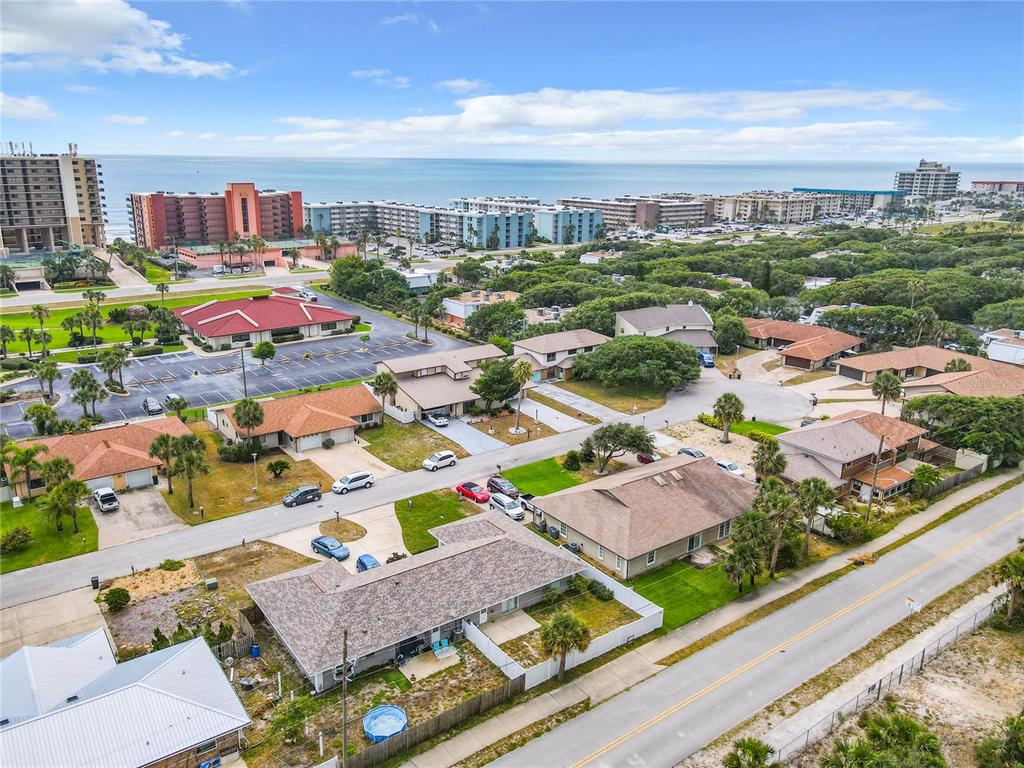 An aerial view shows a residential neighborhood with houses, streets, and the ocean in the distance — 3828 SANDSTONE COURT, NEW SMYRNA BEACH, FL