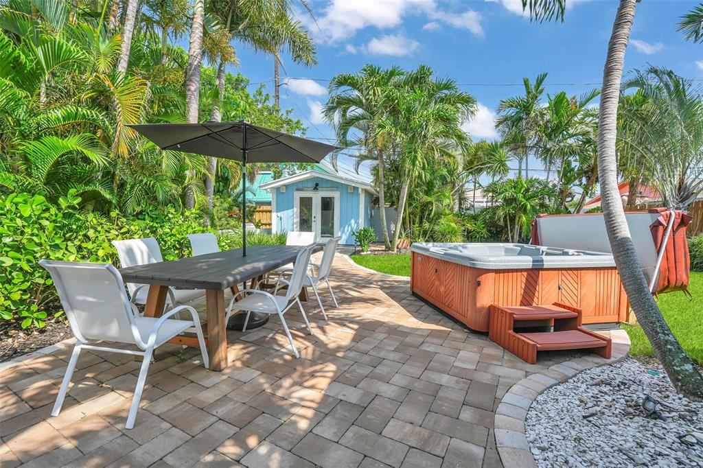 A paved patio features a dining set with an umbrella and a wooden hot tub — 564 70TH AVENUE, ST PETE BEACH, FL