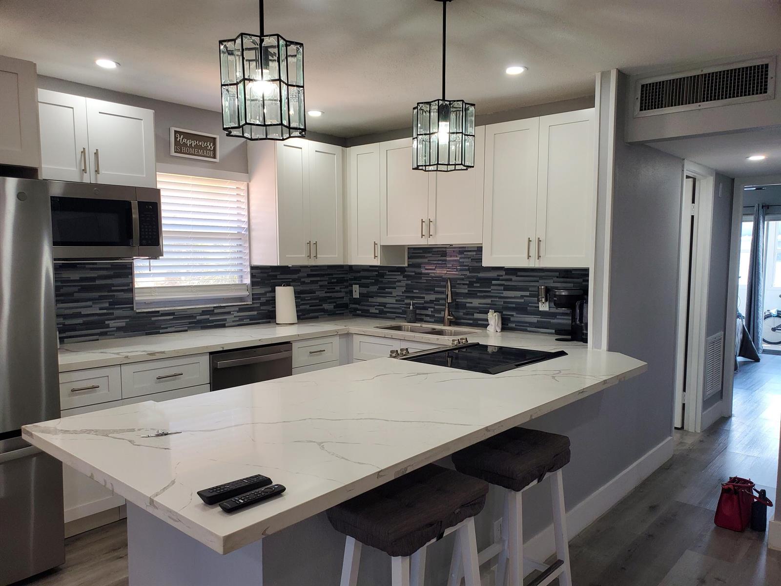 A modern kitchen features white cabinets, marble-look countertops, a dark tile backsplash, and two pendant lights — 564 Saxony L Drive # 564, Delray Beach FL 33446, DELRAY BEACH, FL