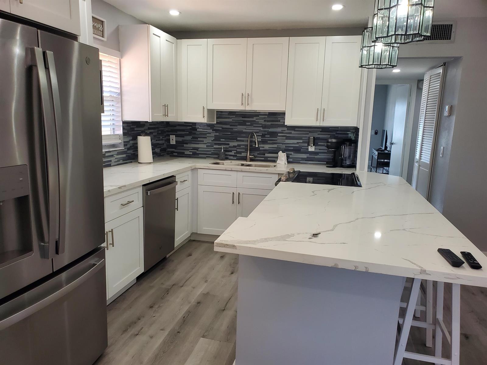 A modern kitchen features white cabinets, marble-look countertops, a blue tiled backsplash, and stainless appliances — 564 Saxony L Drive # 564, Delray Beach FL 33446, DELRAY BEACH, FL