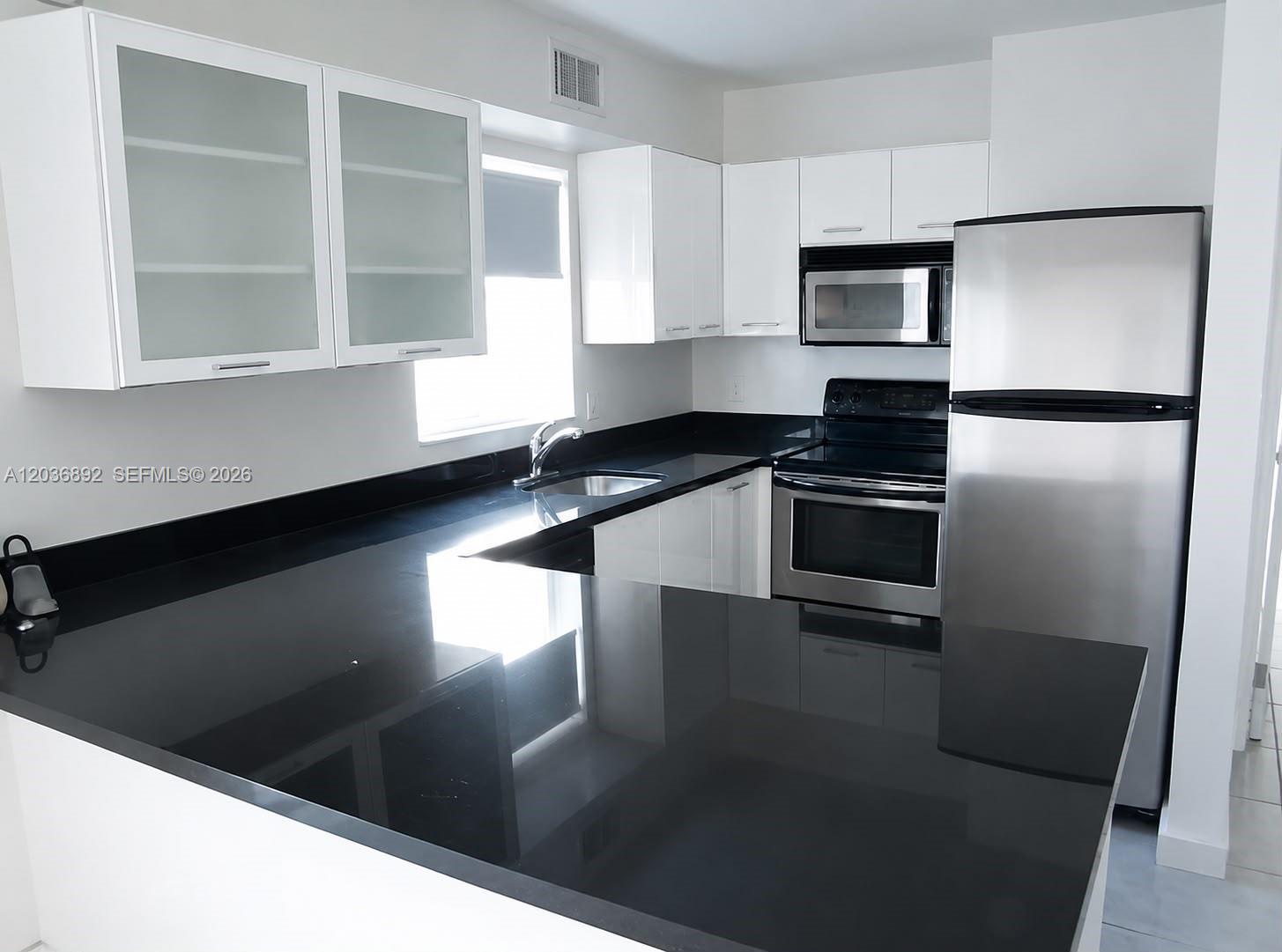 A kitchen features white cabinets, black countertops, and stainless steel appliances — 777 NE 62nd St # C302, Miami FL 33138, MIAMI, FL