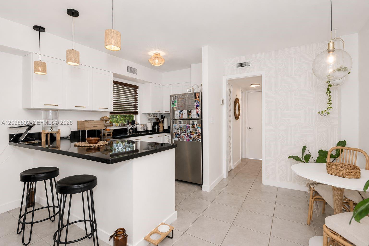 A kitchen features white cabinetry, black countertops, a breakfast bar with stools, and a dining area — 777 NE 62nd St # C302, Miami FL 33138, MIAMI, FL