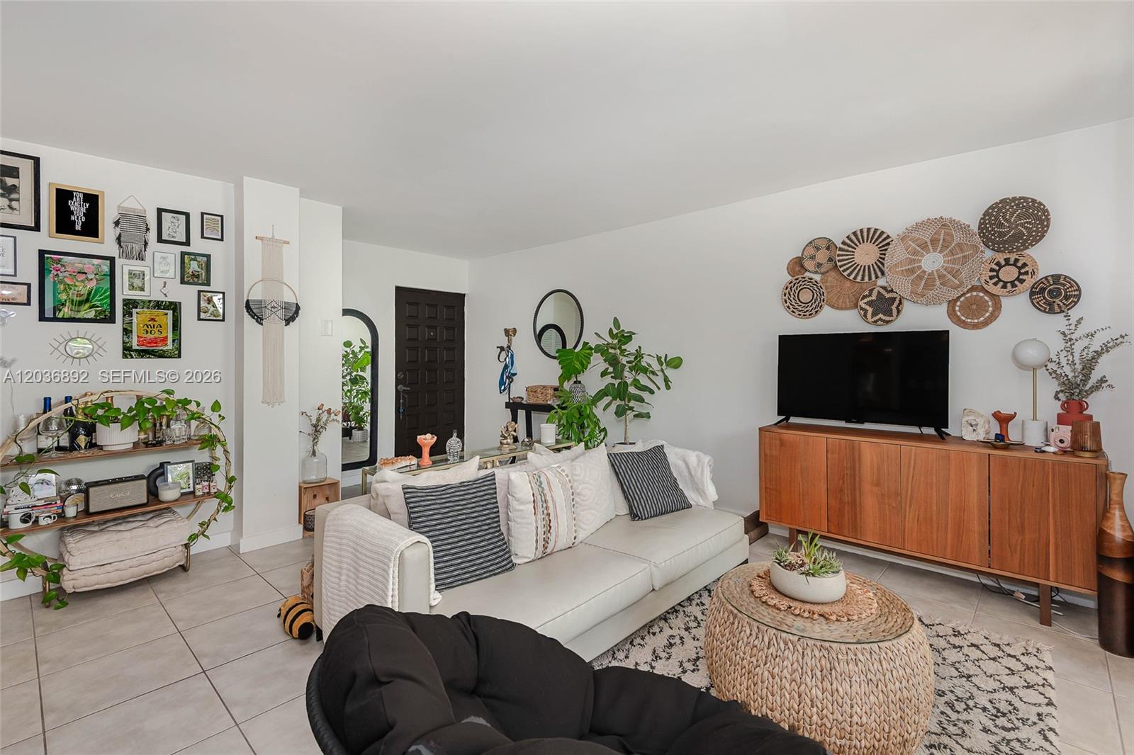 A living room features a white sofa, a wooden media console, and a woven coffee table — 777 NE 62nd St # C302, Miami FL 33138, MIAMI, FL