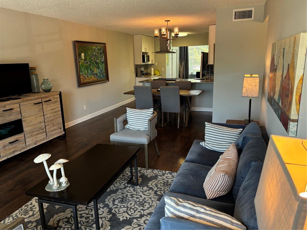 An open-concept living and dining area features dark wood floors, a sofa, and kitchen access — 2456 ECUADORIAN WAY UNIT 42, CLEARWATER, FL