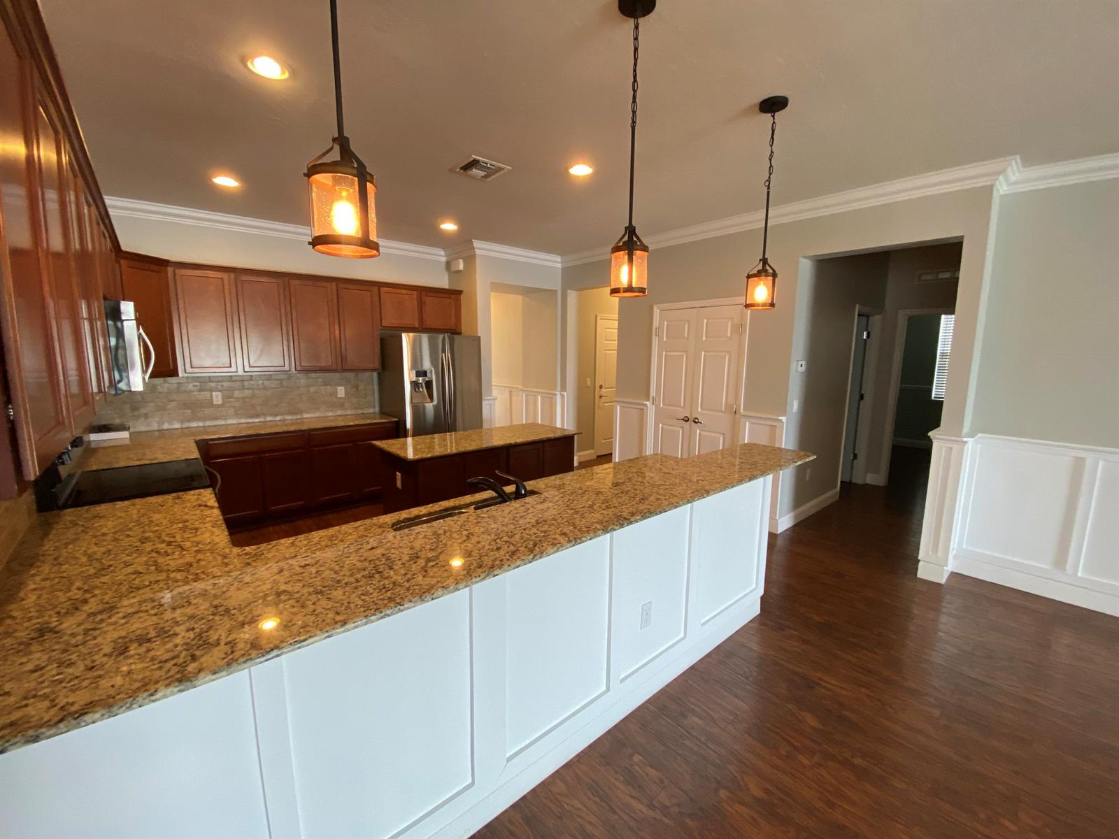 A kitchen features wood cabinets, granite countertops, a center island, and white wainscoting — 9238 Wrangler Drive # L, Wellington FL 33467, WELLINGTON, FL