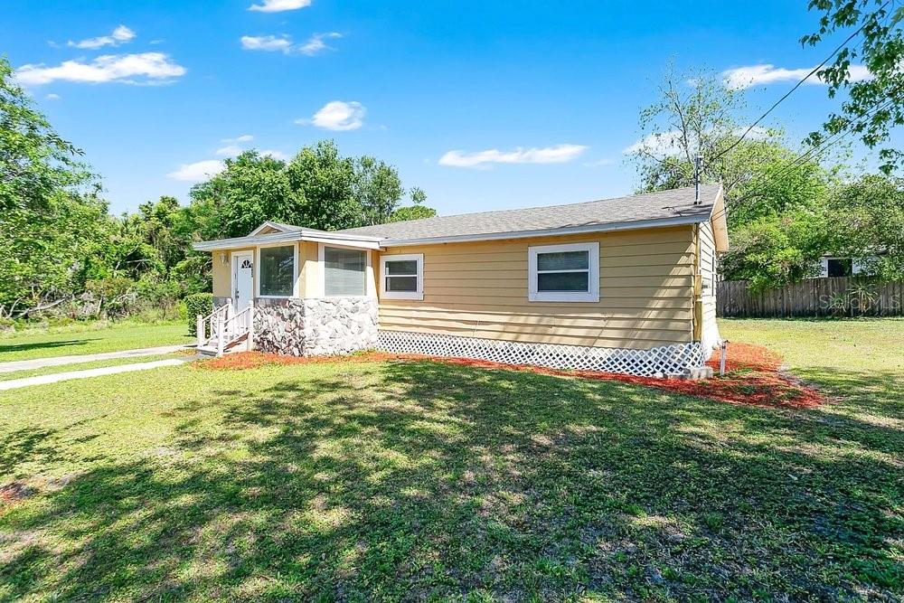 A single-story house with yellow horizontal siding, a stone-accented entryway, and a white lattice foundation — 595 3RD STREET, OVIEDO, FL