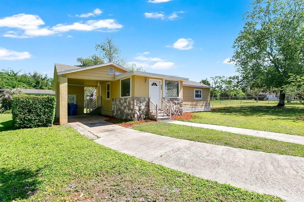 A yellow single-story house features a stone facade, a front porch, and an attached carport — 595 3RD STREET, OVIEDO, FL