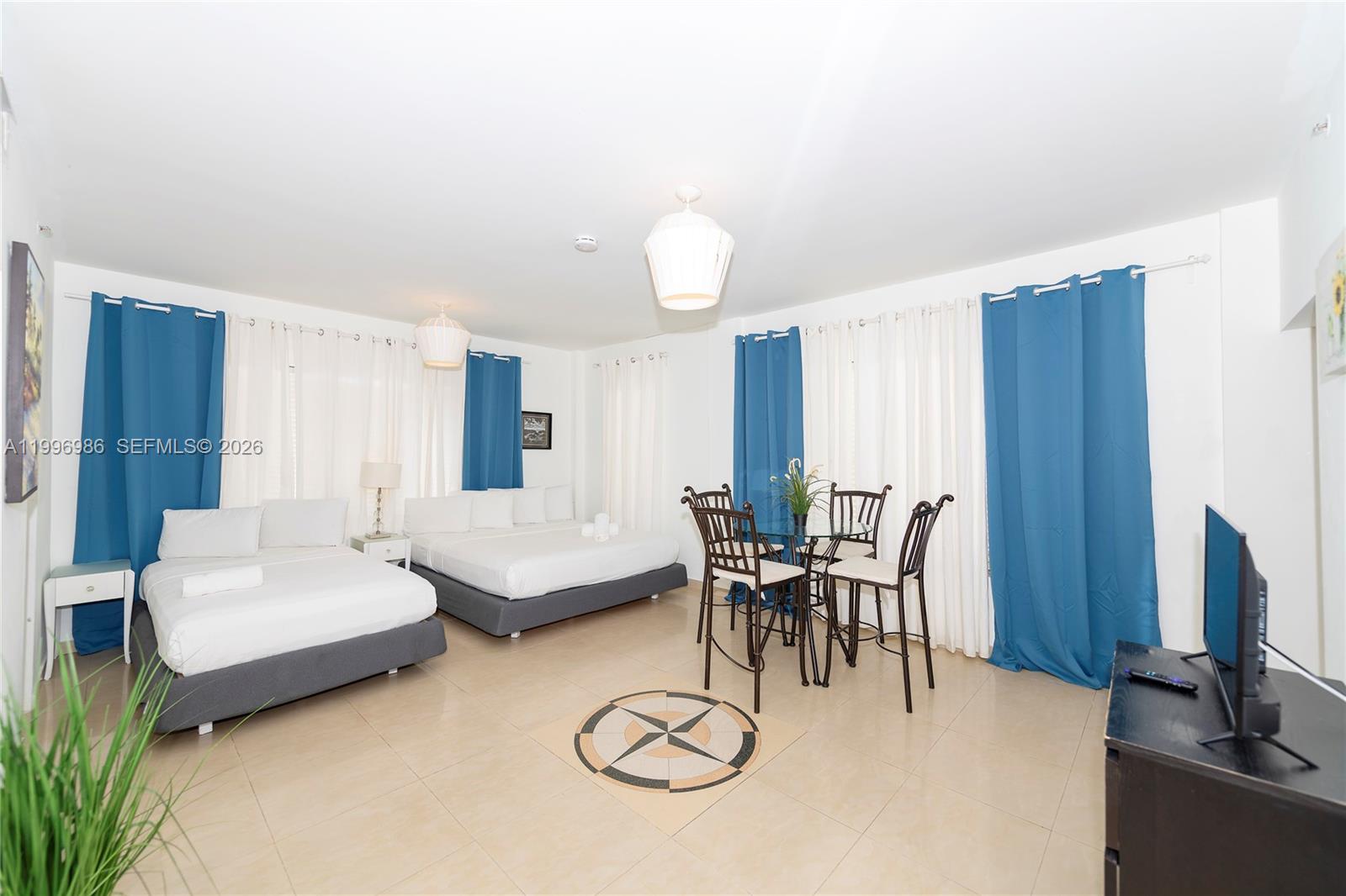 A hotel-style room features two beds, a small dining set, and blue curtains — 918 Ocean Dr # 203, Miami Beach FL 33139, MIAMI BEACH, FL
