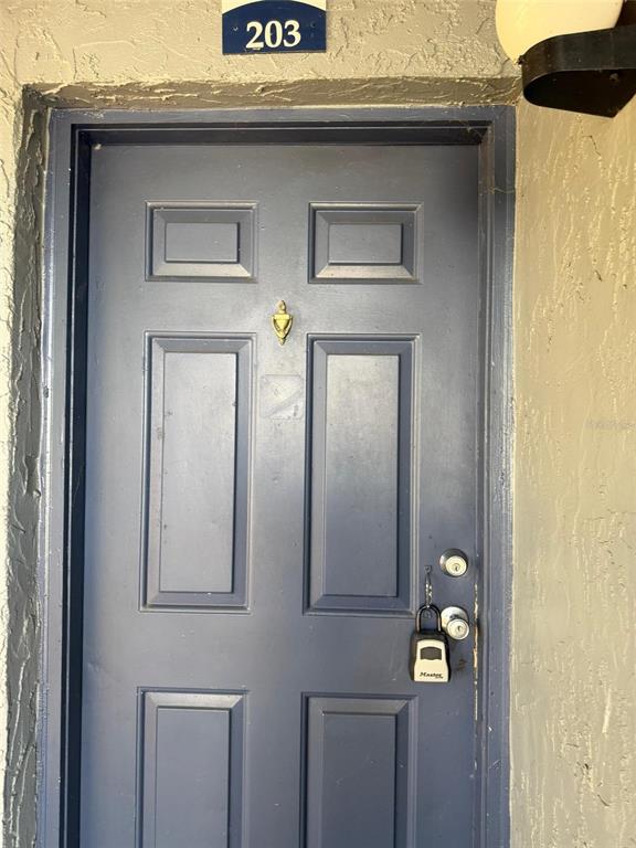 A blue exterior door with a brass knocker and a lockbox hangs under unit number 203 — 3831 NAUTICAL WAY UNIT 203, KISSIMMEE, FL