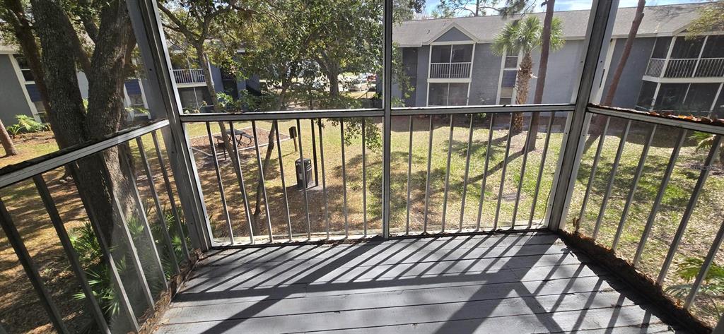 A screened-in balcony overlooks a grassy courtyard with trees and a neighboring apartment building — 3831 NAUTICAL WAY UNIT 203, KISSIMMEE, FL