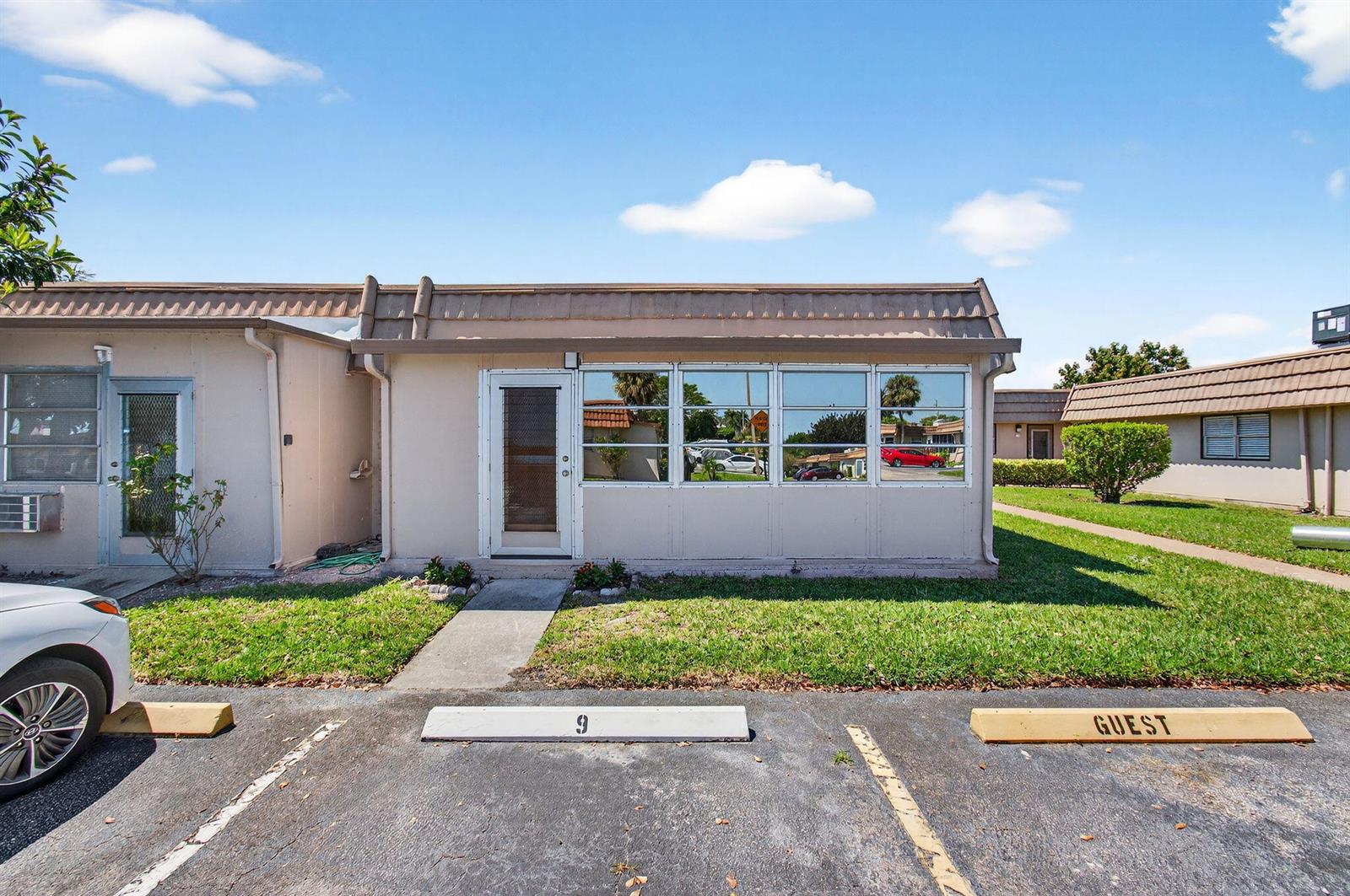 A single-story residential unit with a glass-enclosed porch and assigned parking spaces in front — 225 Seville Boulevard # J, Delray Beach FL 33446, DELRAY BEACH, FL