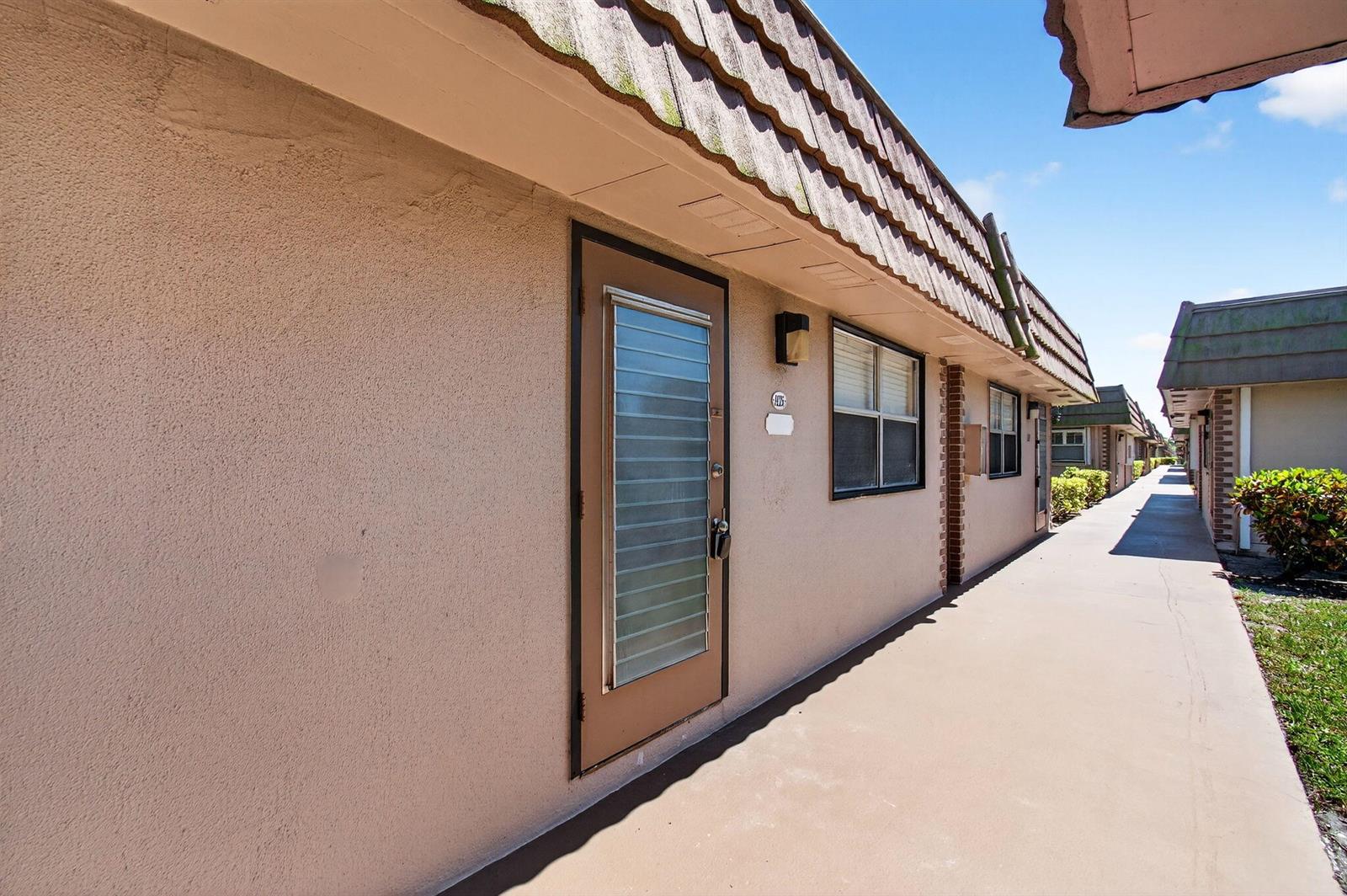 A beige stucco exterior of a single-story apartment building with a brown tiled roof — 225 Seville Boulevard # J, Delray Beach FL 33446, DELRAY BEACH, FL