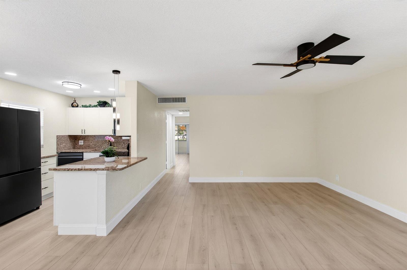An open-concept living area features light wood-look flooring, a ceiling fan, and a kitchen peninsula — 225 Seville Boulevard # J, Delray Beach FL 33446, DELRAY BEACH, FL