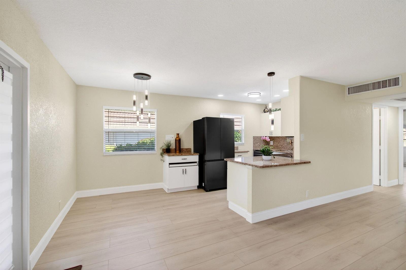 A kitchen and dining area with light wood floors, a black refrigerator, and granite countertops — 225 Seville Boulevard # J, Delray Beach FL 33446, DELRAY BEACH, FL
