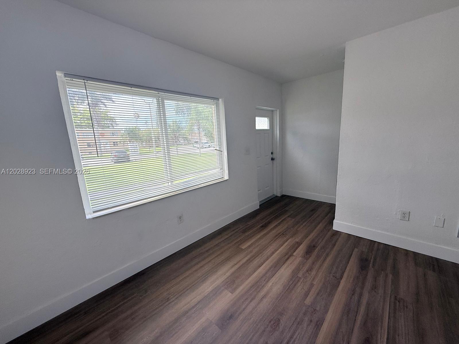 A room with white walls, wood-look flooring, a large window with blinds, and a door — 209 NW 84th St # 209, Miami FL 33150, MIAMI, FL