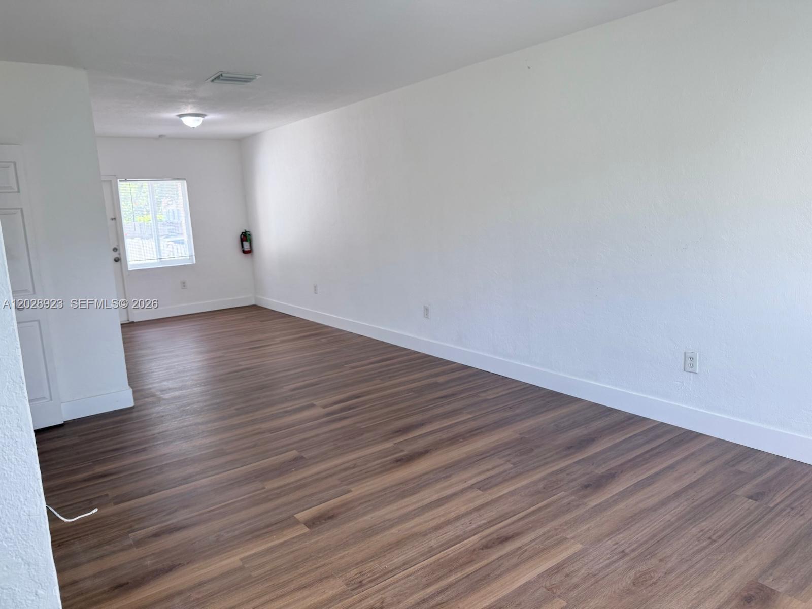 An empty room features white walls, wood-look flooring, a window, and a fire extinguisher — 209 NW 84th St # 209, Miami FL 33150, MIAMI, FL