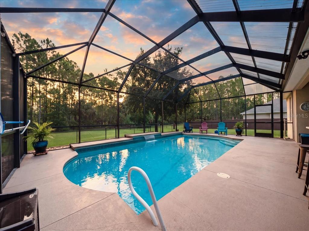 A screened-in swimming pool with a waterfall feature and patio area at sunset — 3095 FAWN LAKE BOULEVARD, MIMS, FL