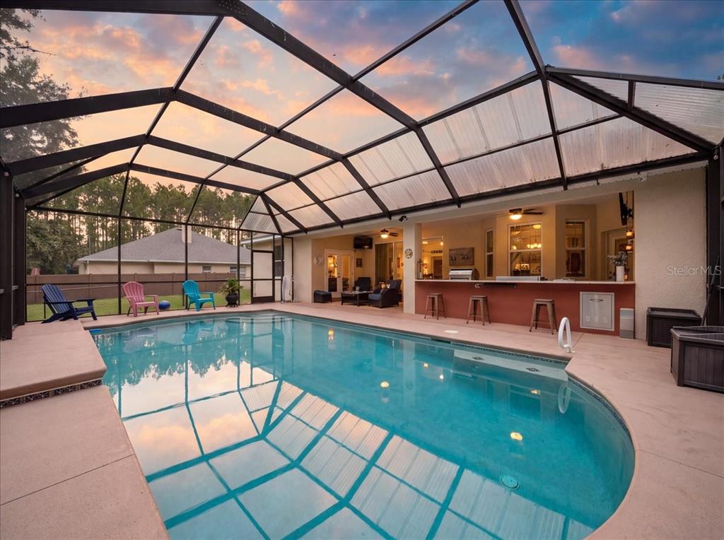 A screened-in swimming pool patio features a built-in outdoor bar with stools and seating — 3095 FAWN LAKE BOULEVARD, MIMS, FL