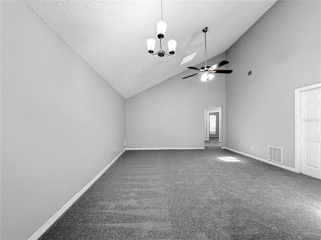 A spacious room with gray carpet, vaulted ceilings, a ceiling fan, and a light fixture — 1854 ALBERTA COURT N, MIDDLEBURG, FL