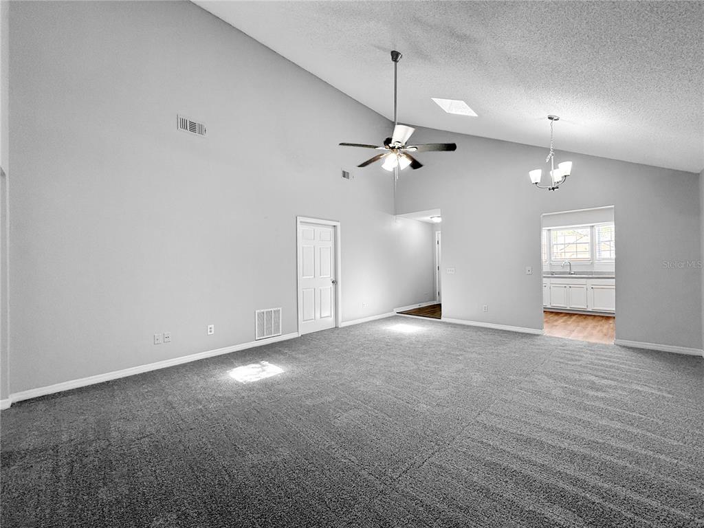 A spacious living room features gray carpeting, vaulted ceilings, a ceiling fan, and a chandelier — 1854 ALBERTA COURT N, MIDDLEBURG, FL