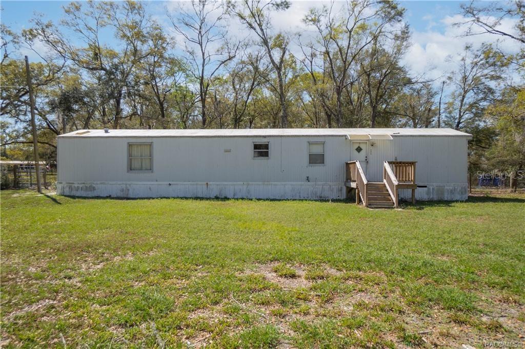 A single-wide mobile home with white siding sits on a grassy lot with trees — 5590 NW 76TH AVENUE, CHIEFLAND, FL