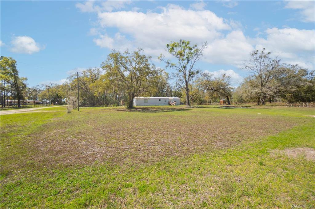 A single-story mobile home sits on a large, grassy lot with several mature trees — 5590 NW 76TH AVENUE, CHIEFLAND, FL