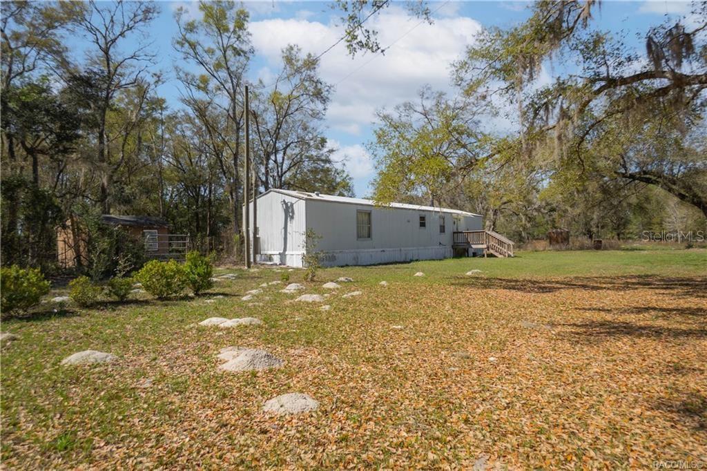 A single-story mobile home sits on a grassy lot surrounded by trees — 5590 NW 76TH AVENUE, CHIEFLAND, FL