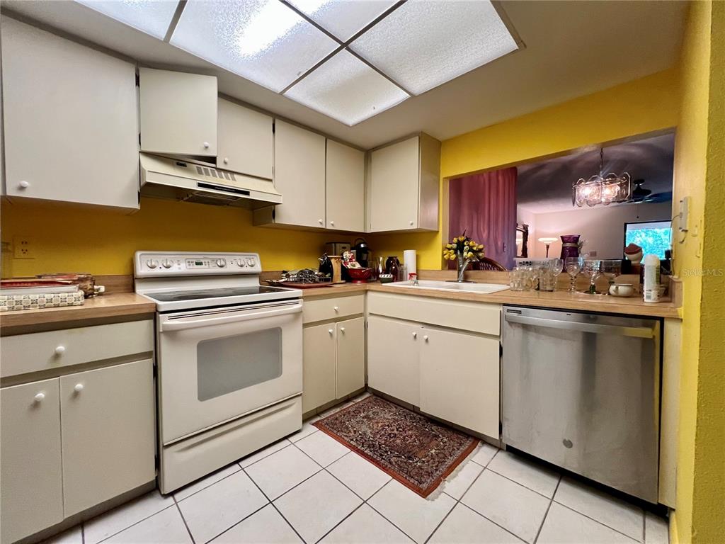 A kitchen features white cabinets, a white stove, a stainless steel dishwasher, and yellow walls — 2650 COUNTRYSIDE BOULEVARD UNIT B302, CLEARWATER, FL