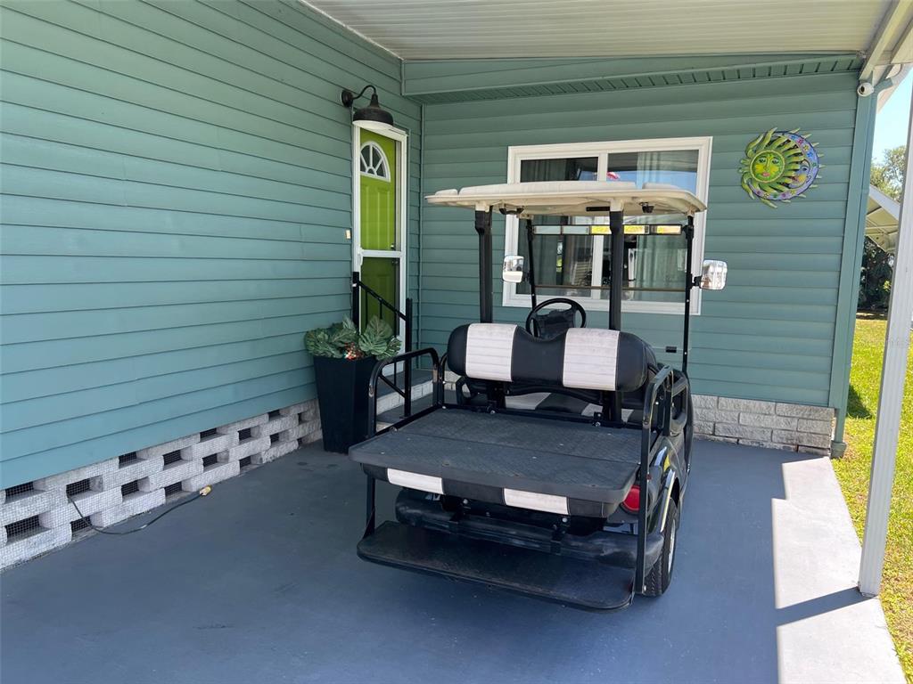 A golf cart is parked on a covered patio next to a teal house — 13225 101ST STREET UNIT 356, LARGO, FL