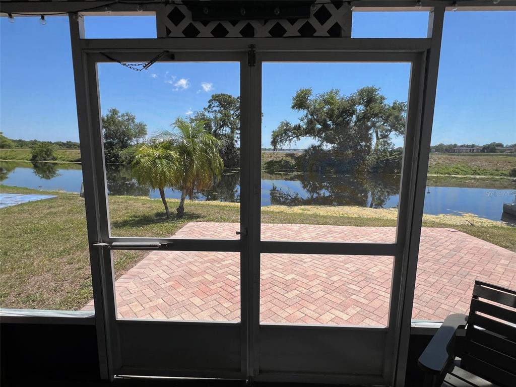 A view through a screened door looking out onto a brick patio and a pond — 13225 101ST STREET UNIT 356, LARGO, FL