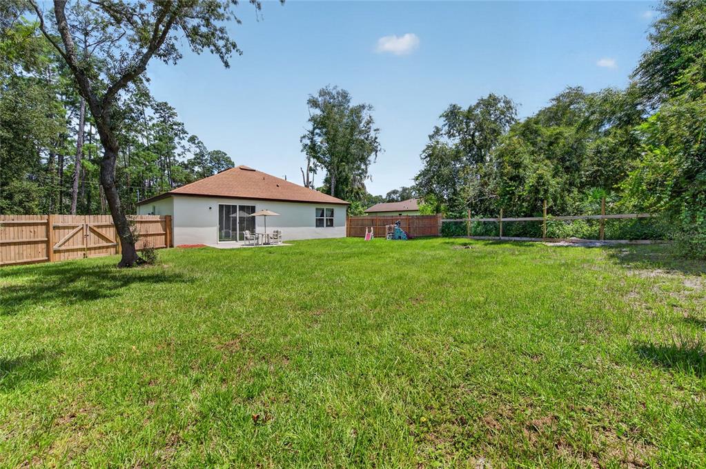 A fenced backyard with a grassy lawn and a single-story house with a patio — 1462 5TH AVENUE, DELAND, FL