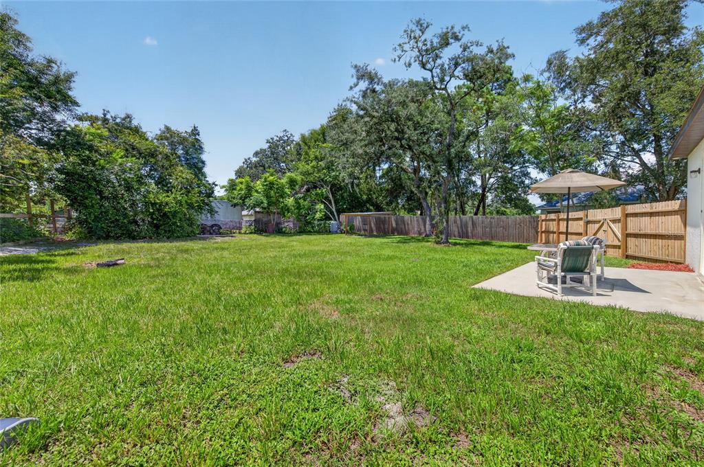 A grassy backyard features a concrete patio with a table, chairs, and a patio umbrella — 1462 5TH AVENUE, DELAND, FL
