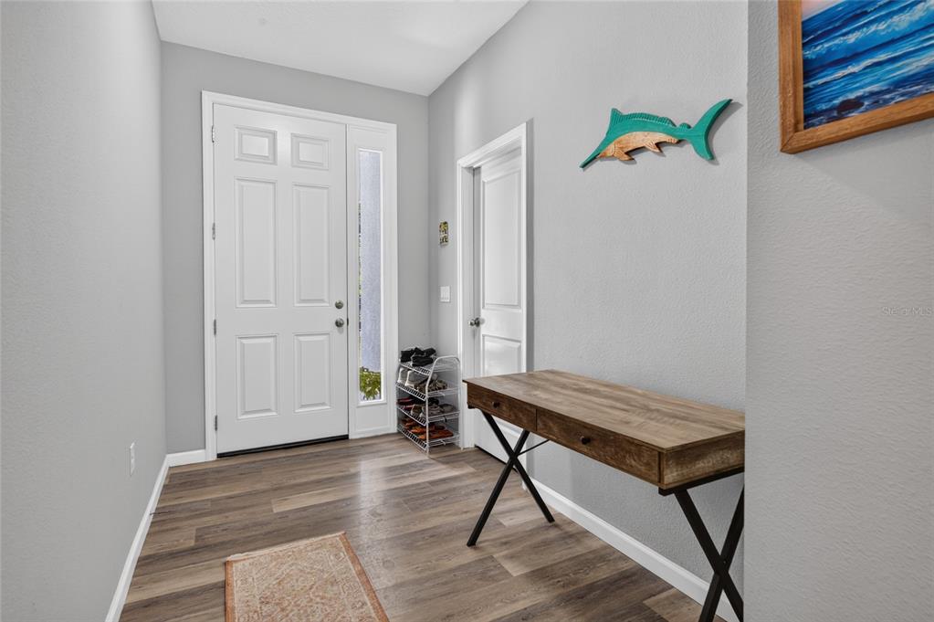 An entryway features wood-look flooring, a white front door, a console table, and wall decor — 1462 5TH AVENUE, DELAND, FL