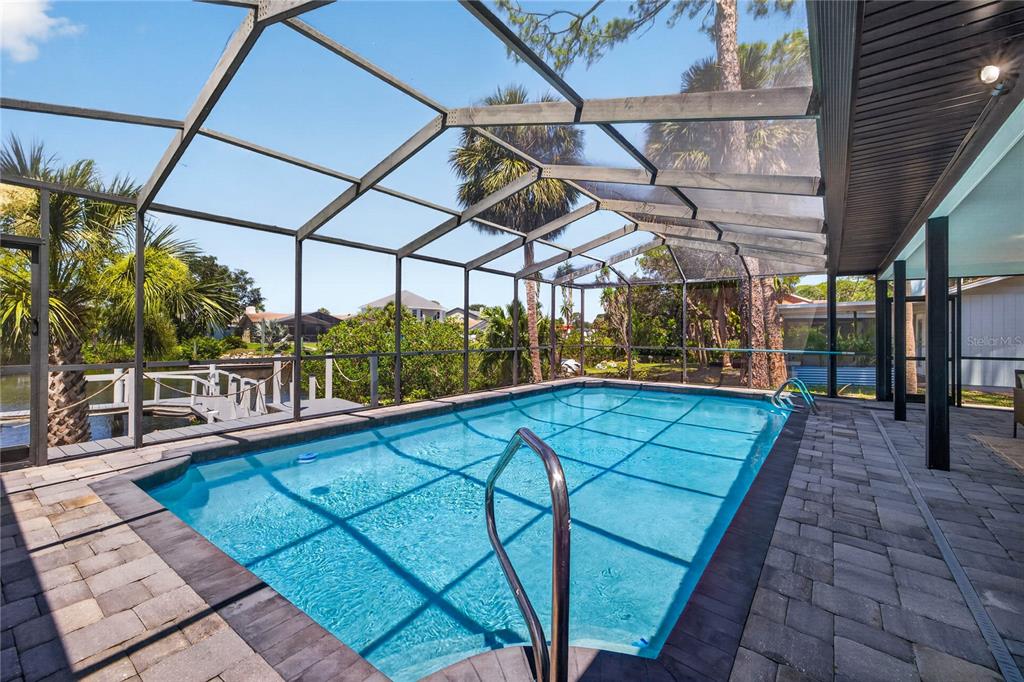 A rectangular swimming pool enclosed by a screened lanai with stone pavers and water views — 4346 MARINE PARKWAY, NEW PORT RICHEY, FL