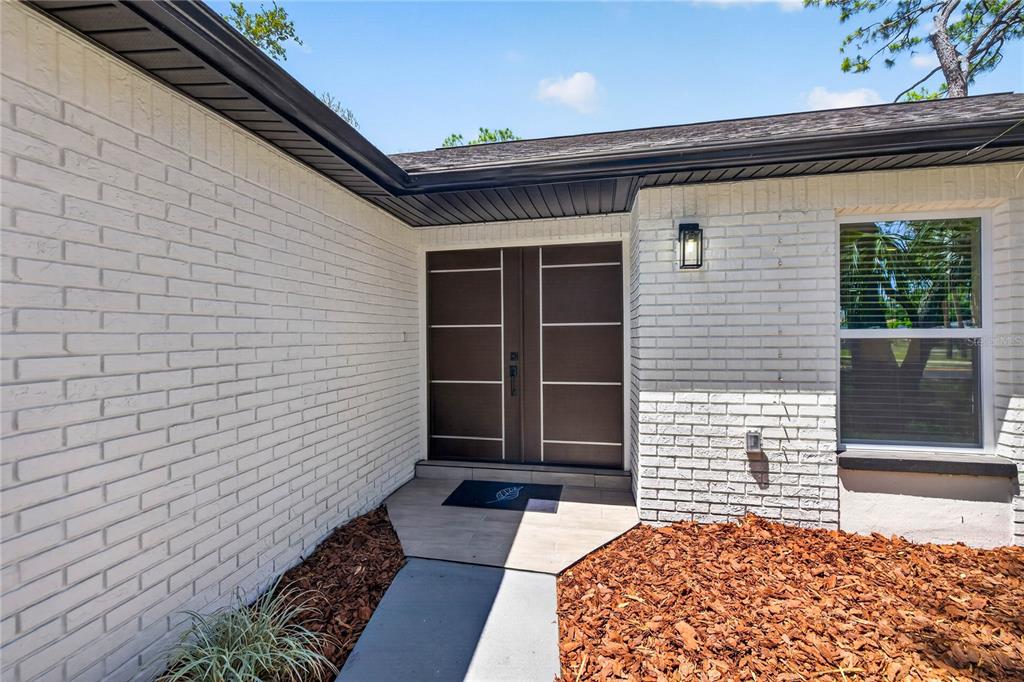 A white brick exterior features a modern double front door and a tiled entryway — 4346 MARINE PARKWAY, NEW PORT RICHEY, FL