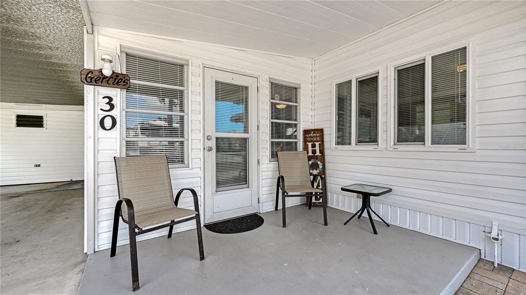 A covered porch with two chairs, a small table, and a white exterior wall — 10315 CORTEZ ROAD W UNIT 30-5, BRADENTON, FL