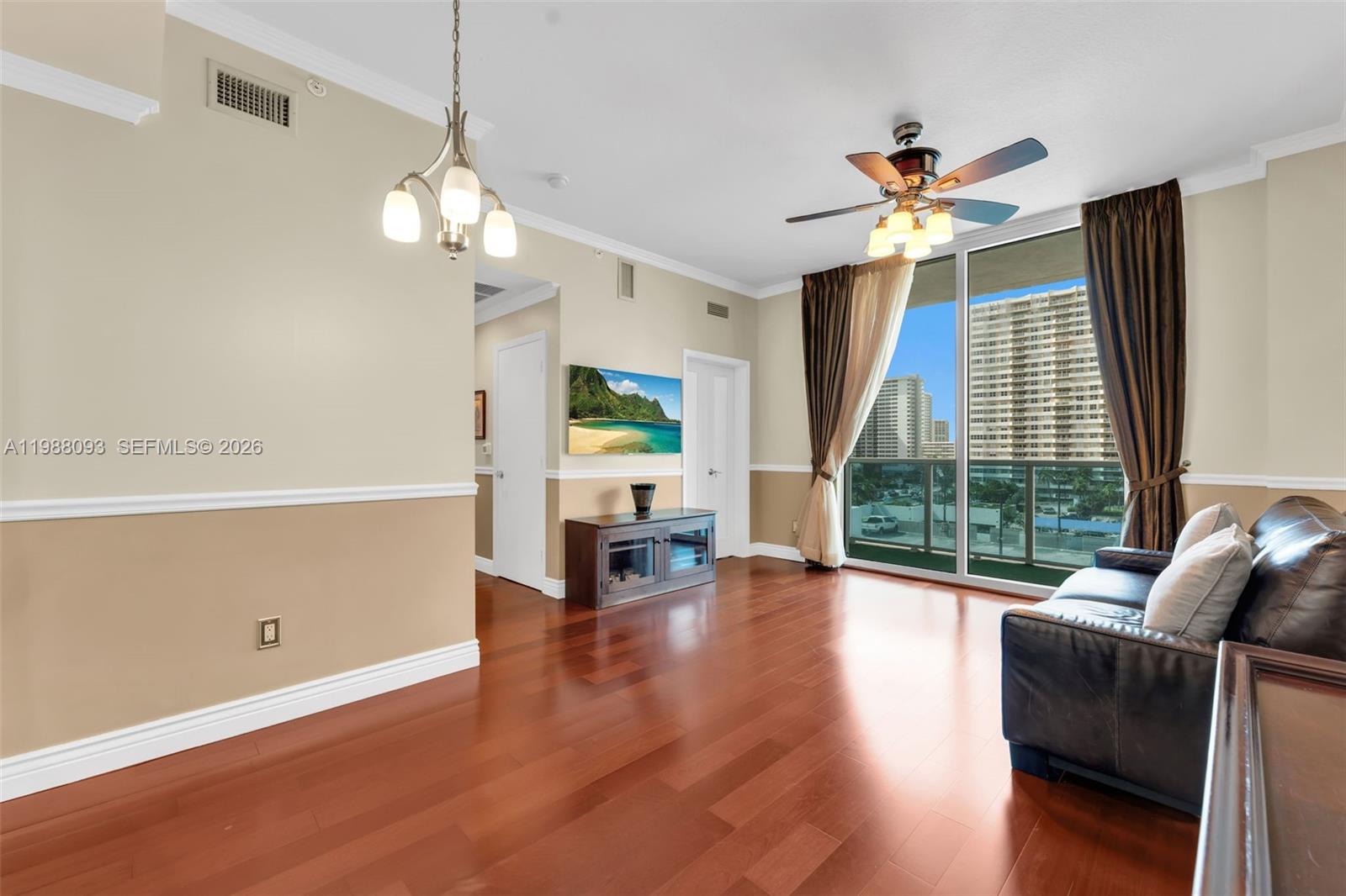 A living room features hardwood floors, a ceiling fan, a chandelier, and a balcony view — 1945 S Ocean Dr # 604, Hallandale Beach FL 33009, HALLANDALE BEACH, FL