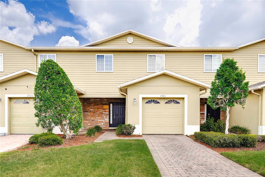 A two-story townhouse exterior features tan siding, stone accents, and two attached garages — 1921 CHATHAM PLACE DRIVE, ORLANDO, FL