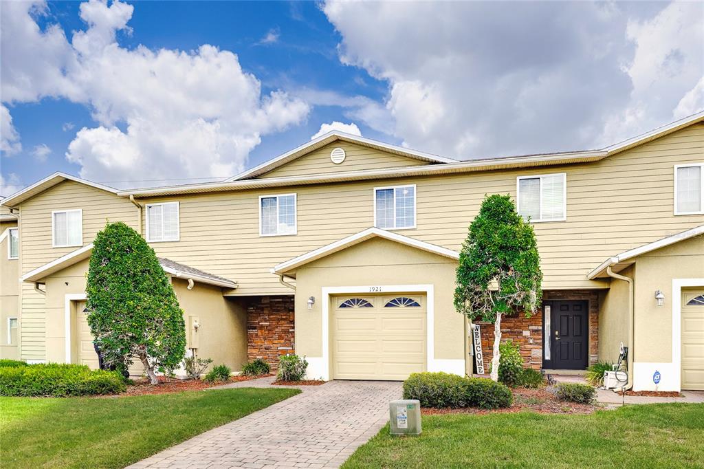 A two-story townhouse with tan siding, a stone facade, and a paved driveway — 1921 CHATHAM PLACE DRIVE, ORLANDO, FL