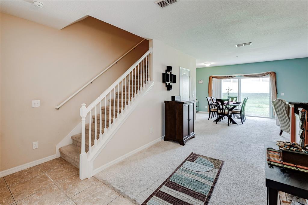 A carpeted living area features a staircase with white railings and a dining room beyond — 1921 CHATHAM PLACE DRIVE, ORLANDO, FL
