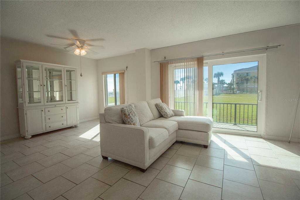 A living room with a white sectional sofa, a hutch, tile floors, and sliding glass doors — 3600 S OCEAN SHORE BOULEVARD UNIT 115, FLAGLER BEACH, FL