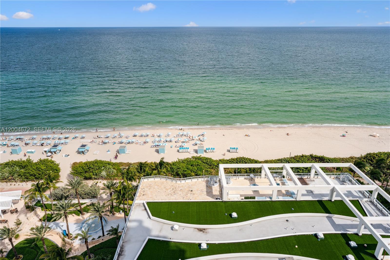An aerial view shows a building rooftop with green turf and a beach with umbrellas — 6799 Collins Ave # 1602, Miami Beach FL 33141, MIAMI BEACH, FL
