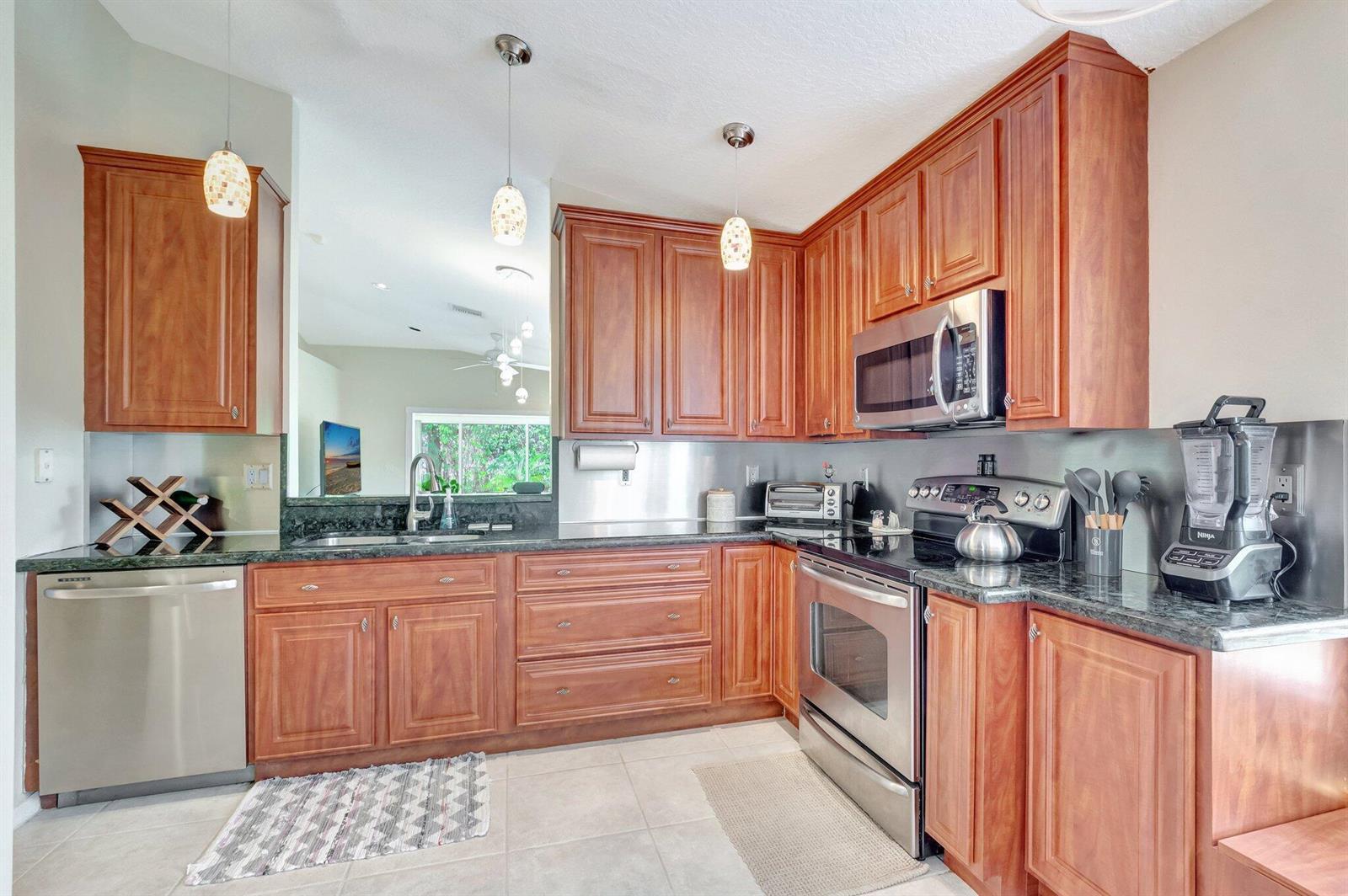 A kitchen features cherry wood cabinets, stainless steel appliances, and dark granite countertops — 14211 W La Sedona Circle, Delray Beach FL 33484, DELRAY BEACH, FL