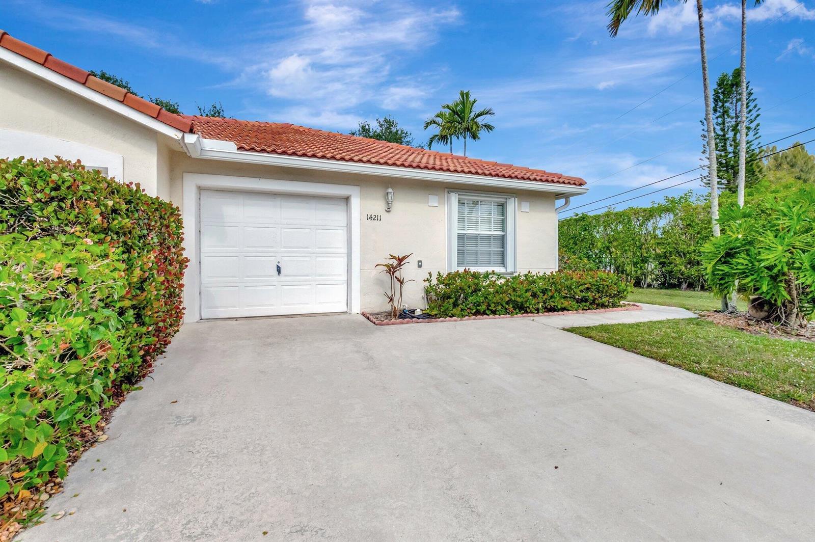The exterior of a single-story house features a white garage door and a tiled roof — 14211 W La Sedona Circle, Delray Beach FL 33484, DELRAY BEACH, FL