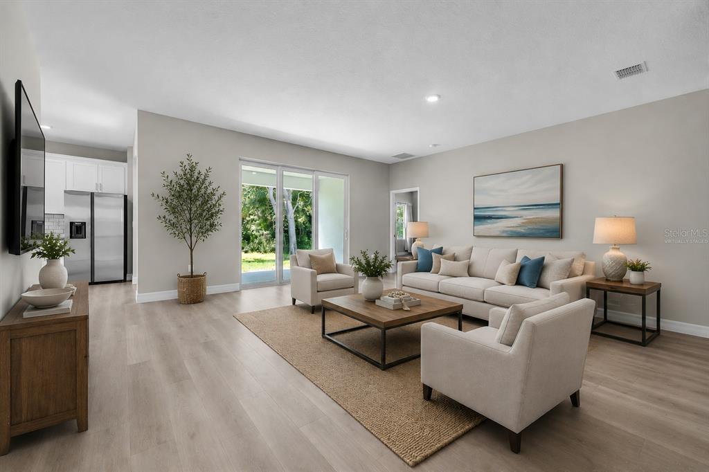 A living room features light wood flooring, a neutral sofa, two armchairs, and sliding glass doors — 27431 NATAL DRIVE, PUNTA GORDA, FL