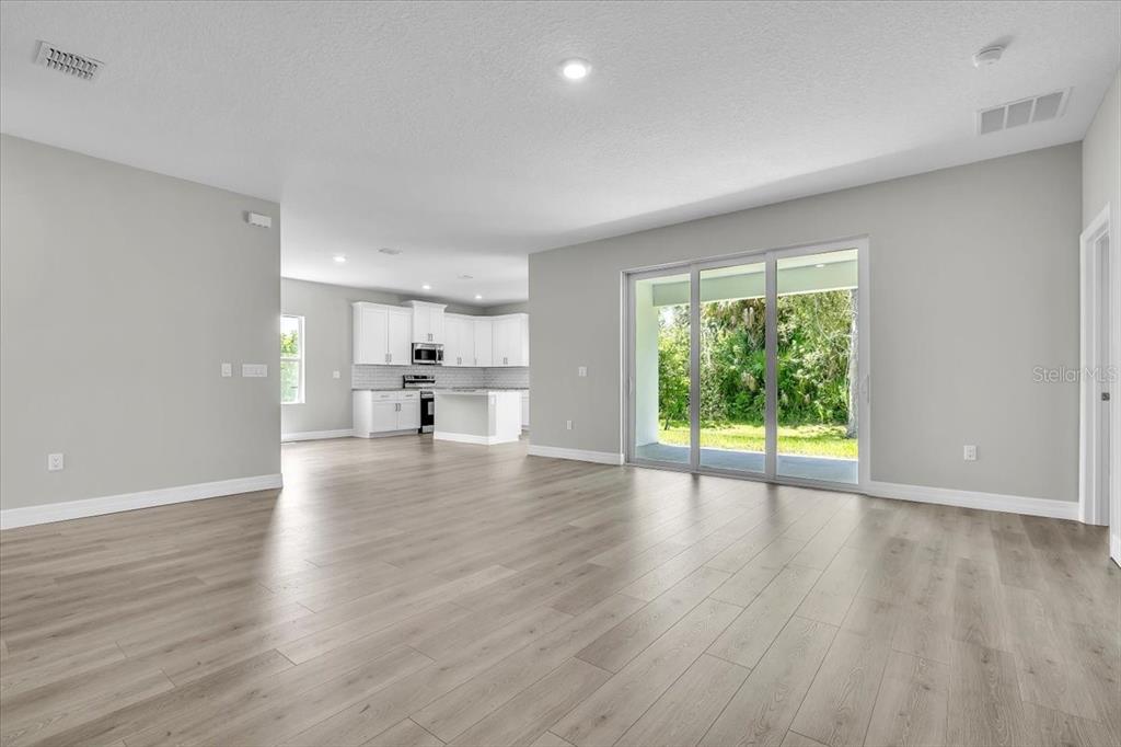 An open-concept living area with light wood-look flooring leads to a kitchen and sliding doors — 27431 NATAL DRIVE, PUNTA GORDA, FL