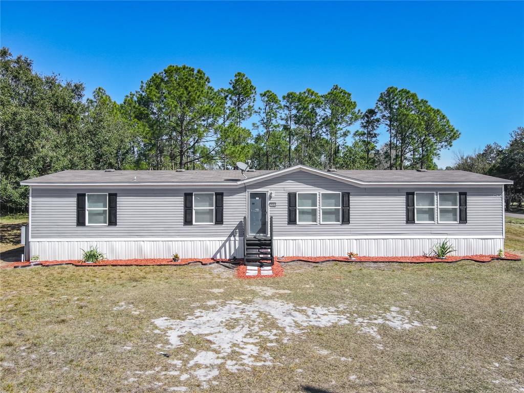 A single-story manufactured home with gray siding and black shutters sits on a grassy lot — 3564 REAGAN BOULEVARD, LAKE WALES, FL