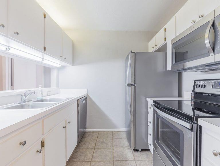 A galley kitchen features white cabinets, stainless steel appliances, and light-colored tile flooring — 4000 SW 23RD STREET UNIT 4-103 #3, GAINESVILLE, FL